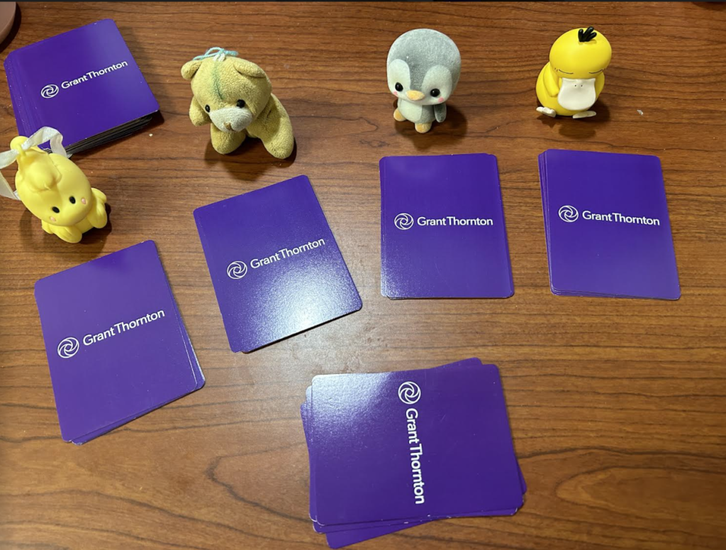 The cards are now distributed by a sample amount. The rest of the deck is in the background, and there are now the small toys placed by four of the distributed piles. The cards have the front of the cards displaying the suits face down.