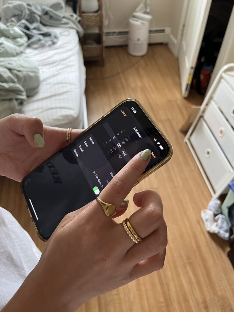 A person is on their Iphone, they are currently on the time app setting an alarm for 8:00 am.