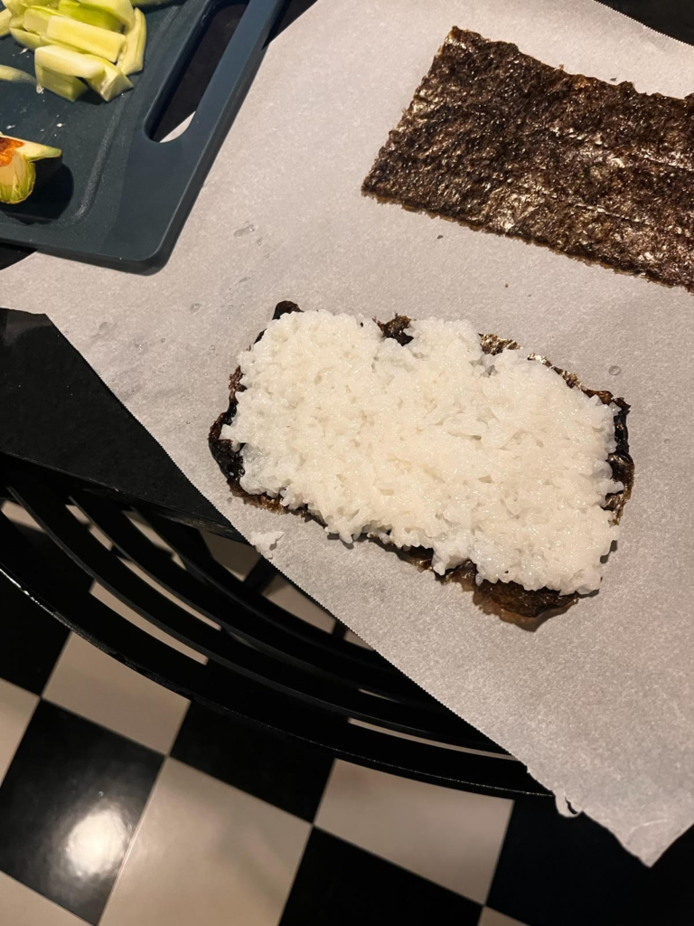 one torn piece of seaweed placed horizontally on the parchment paper with a thin layer of rice on top